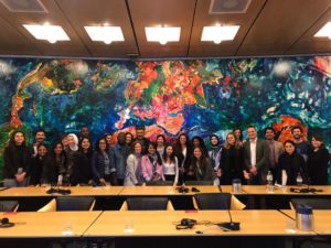 A group of students standing before a colourful wall with a world map painting